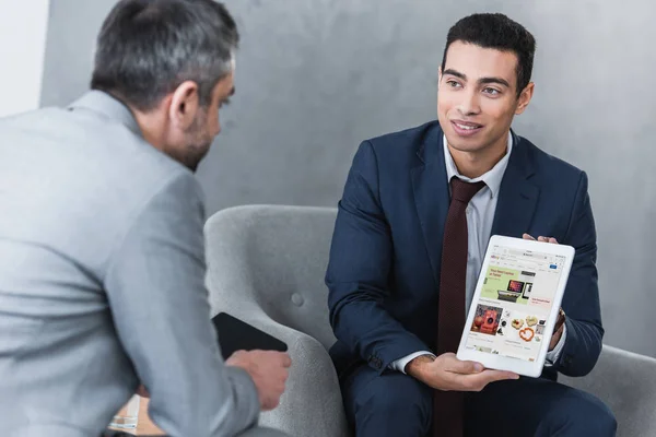 Smiling young businessman showing digital tablet with ebay app to colleague — Stock Photo