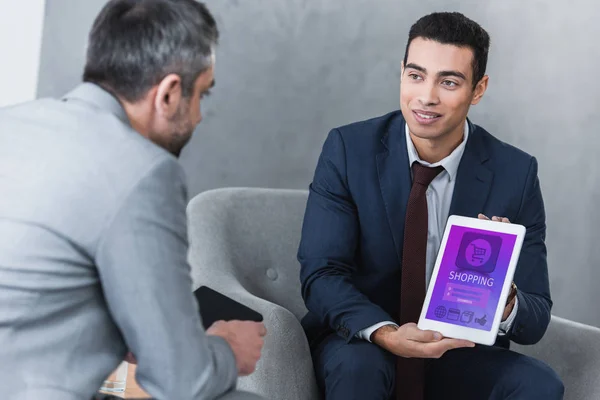 Jeune homme d'affaires souriant montrant tablette numérique avec application de magasinage à un collègue — Photo de stock