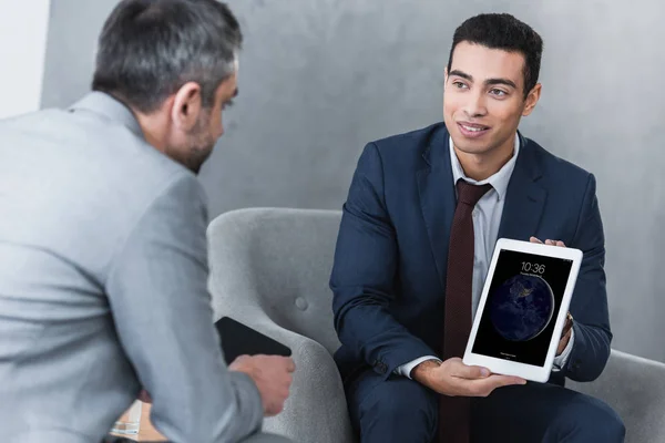 Smiling young businessman showing digital tablet to colleague — Stock Photo