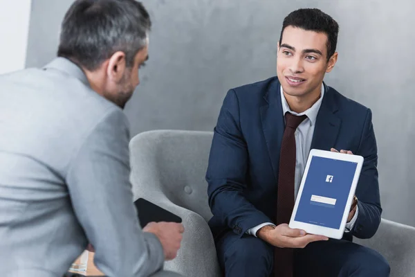 Lächelnder junger Geschäftsmann zeigt Kollegen digitales Tablet mit Facebook-App — Stockfoto