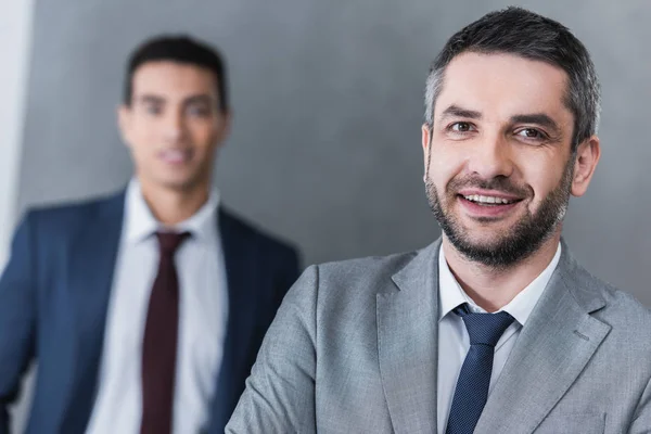 Selektiver Fokus zweier gutaussehender Geschäftsleute, die in die Kamera lächeln — Stockfoto