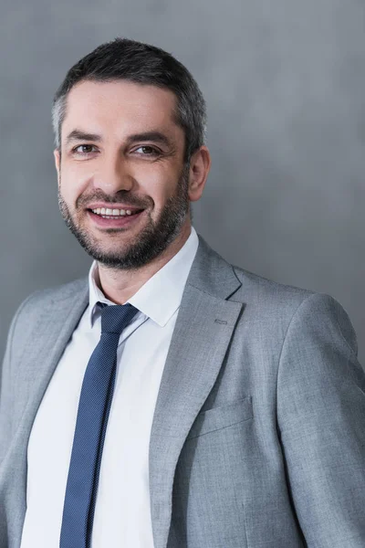 Handsome happy businessman in formal wear smiling at camera on grey — Stock Photo