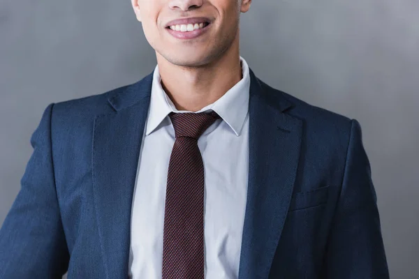 Recortado disparo de sonriente joven hombre de negocios en ropa formal en gris - foto de stock