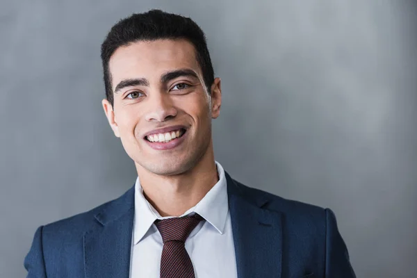 Porträt eines hübschen jungen Geschäftsmannes, der in grau in die Kamera lächelt — Stockfoto