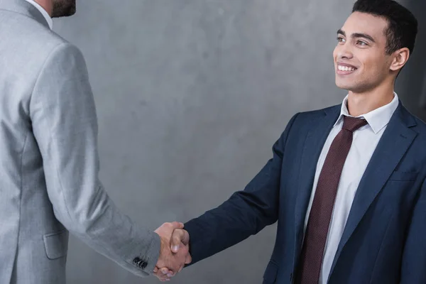 Обрізаний знімок усміхненого молодого бізнесмена, що тремтить руками з колегою на сірому — стокове фото