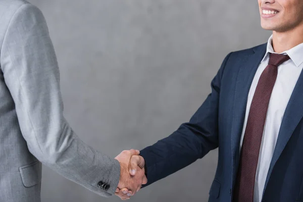Cropped shot of businessmen in formal wear shaking hands on grey — Stock Photo