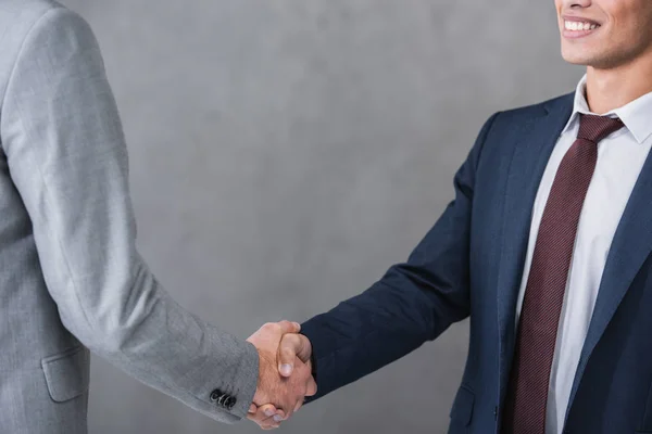 Recortado tiro de los hombres de negocios en formal desgaste apretando las manos en gris - foto de stock