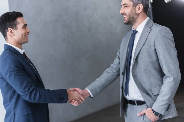 Seitenansicht von Geschäftsleuten, die sich im Amt die Hände schütteln und einander lächeln — Stockfoto