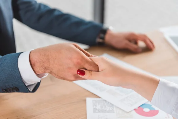 Cropped shot of businessman and businesswoman shaking hands above table with papers — Stock Photo
