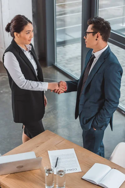 High angle view of young asian business people shaking hands, contract and laptop on table — Stock Photo