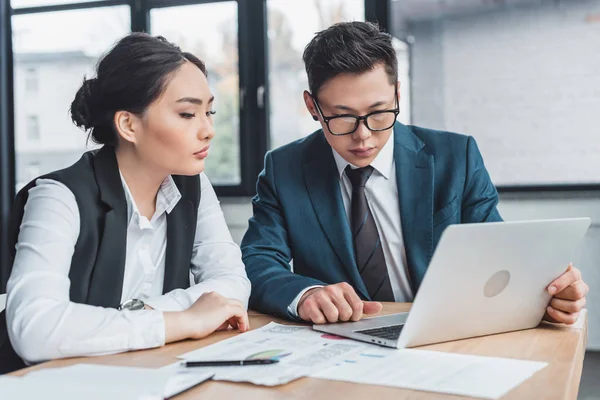 Focused young business colleagues working with laptop and papers in office — Stock Photo