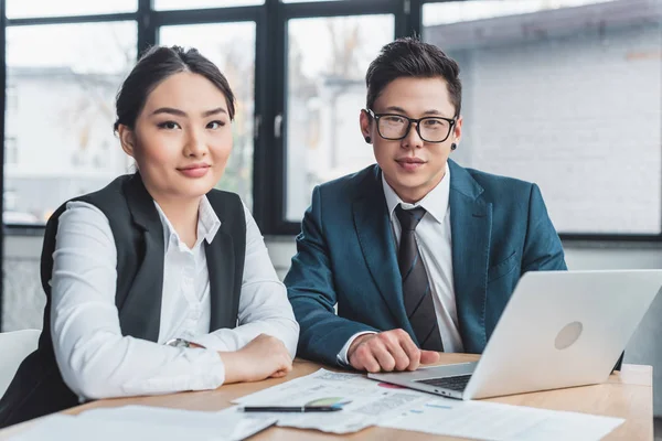 Young kazakh business people sitting at workplace and smiling at camera — Stock Photo