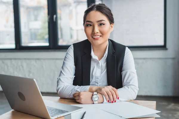 Beautiful young kazakh businesswoman sitting at workplace and smiling at camera in office — Stock Photo