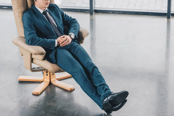 Cropped shot of young businessman in suit sitting in chair at workplace — Stock Photo