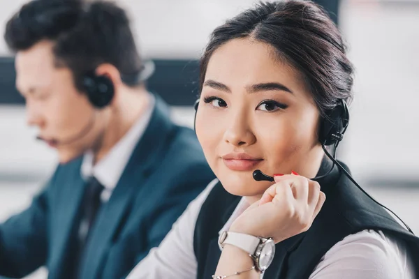 Hermosa joven kazakh mujer en auriculares sonriendo a la cámara en el lugar de trabajo - foto de stock