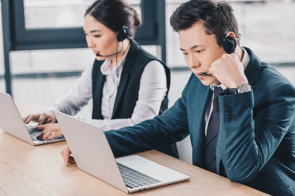 Giovani operatori di call center in auricolari utilizzando computer portatili in ufficio — Foto stock