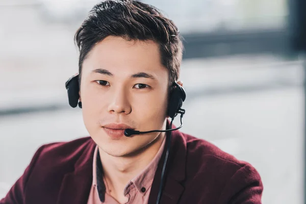 Handsome young asian manager in headset looking at camera in office — Stock Photo