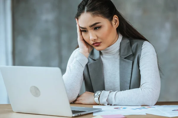 Overworked young businesswoman sitting at workplace and using laptop — Stock Photo