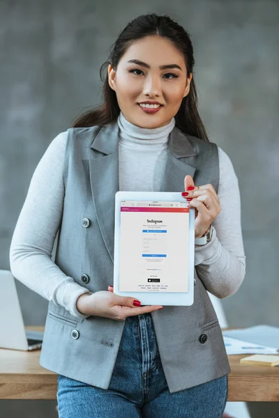 Молодая азиатская бизнесвумен держит цифровой планшет с приложением Instagram и улыбается в камеру — стоковое фото