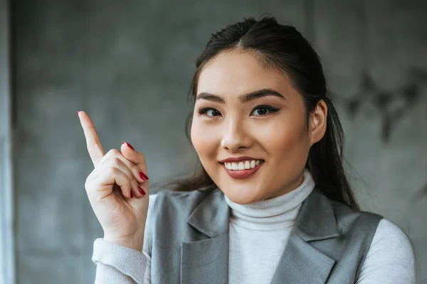 Hermosa mujer de negocios kazakh señalando hacia arriba con el dedo y sonriendo a la cámara - foto de stock