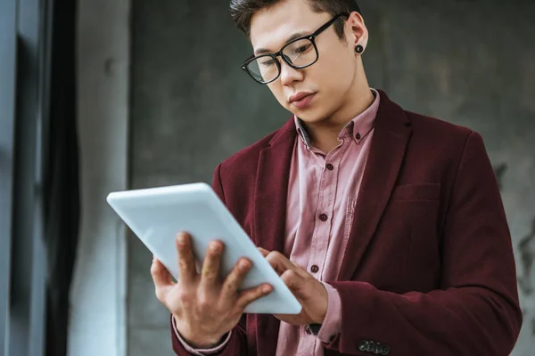 Зосереджений молодий чоловік в окулярах, використовуючи цифровий планшет в офісі — стокове фото