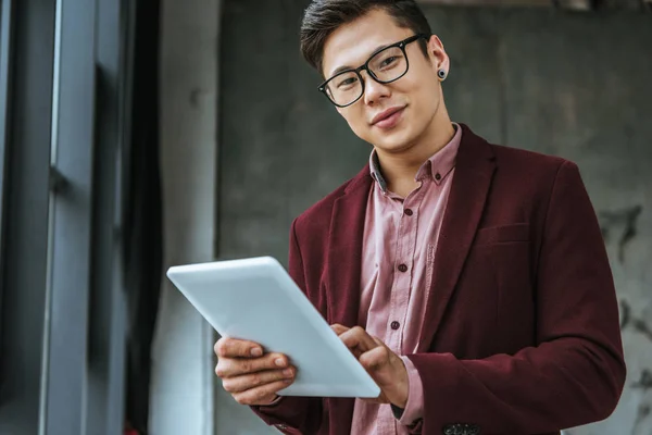 Handsome kazakh businessman in eyeglasses using digital tablet and looking at camera in office — Stock Photo