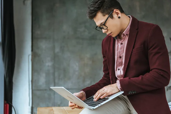 Schöner junger Geschäftsmann mit Brille sitzt und Laptop im Büro benutzt — Stockfoto