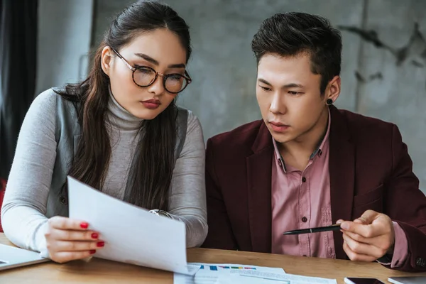 Enfocado jóvenes asiático negocios colegas buscando en los papeles en oficina - foto de stock