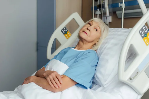 Senior woman with hands crossed lying in bed in hospital — Stock Photo
