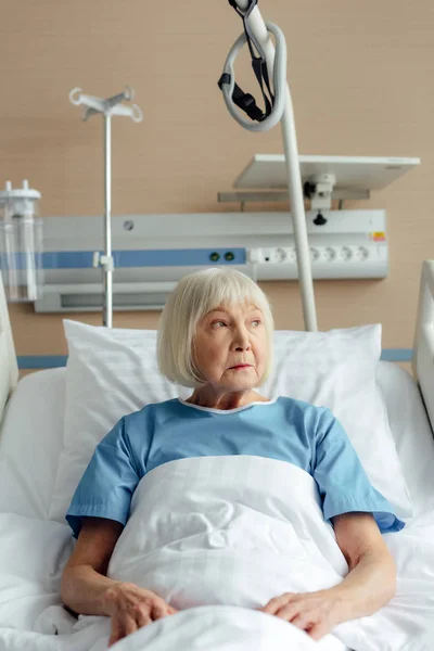 Mujer mayor acostada en la cama en el hospital y mirando hacia otro lado - foto de stock