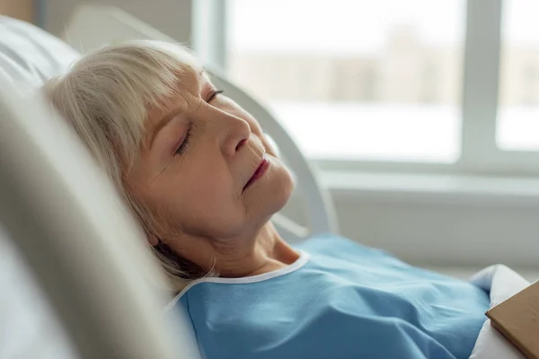 Селективное внимание пожилой женщины с седыми волосами, спящей в больничной койке — стоковое фото