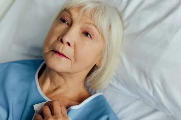 Triste mujer mayor con el pelo gris acostado en la cama en el hospital - foto de stock