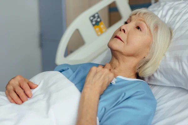 Selektiver Fokus einer einsamen Seniorin, die im Krankenhausbett liegt und weint — Stockfoto