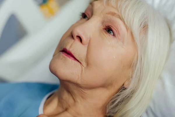 Primer plano de la mujer mayor molesta con el pelo gris acostado en la cama y llorando en el hospital - foto de stock