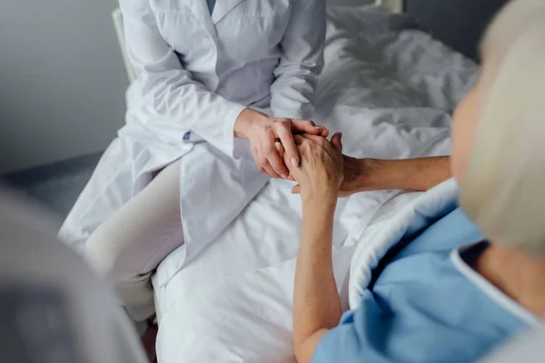 Vue partielle du médecin féminin tenant la main avec une femme âgée couchée au lit à l'hôpital — Photo de stock
