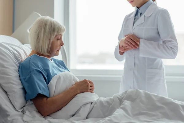 Ärztin berät Seniorin, die im Krankenhausbett liegt — Stockfoto