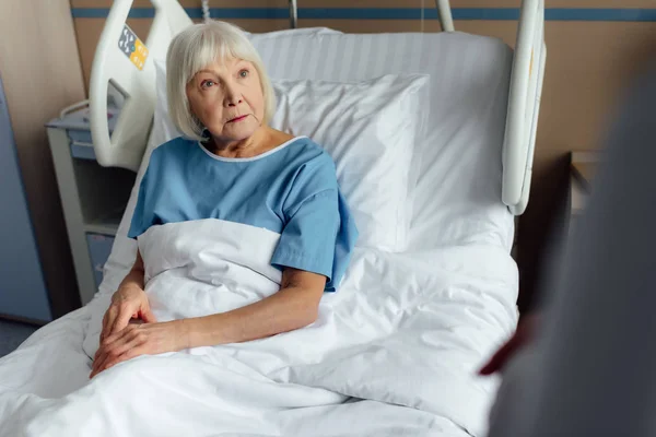 Foco seletivo da mulher idosa triste com cabelos grisalhos deitado na cama do hospital — Fotografia de Stock