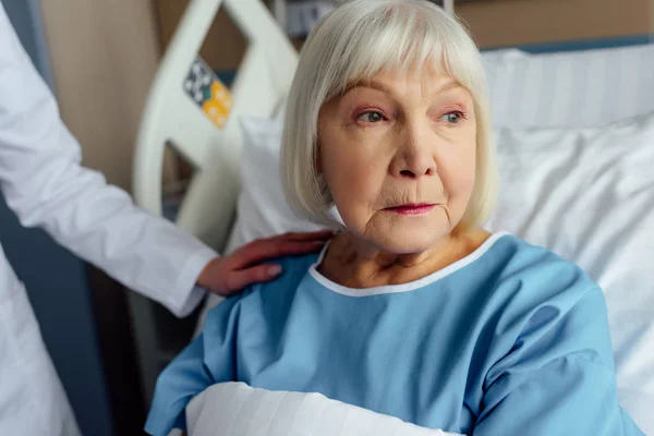 Female doctor consoling worried senior woman lying in hospital bed — Stock Photo