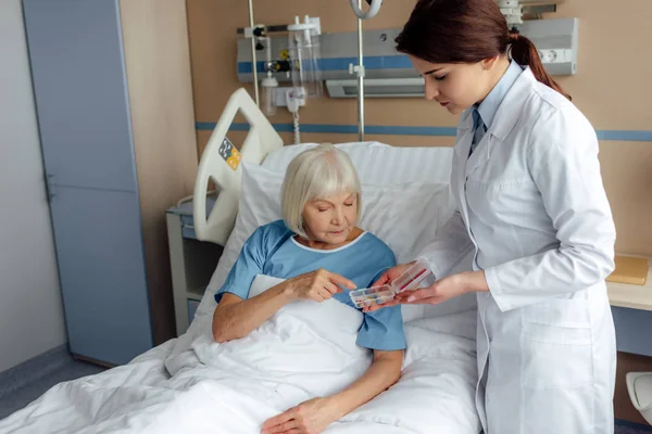 Female doctor giving pills to senior woman lying in hospital bed — Stock Photo