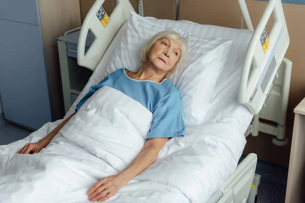 Sad lonely senior woman lying in hospital bed — Stock Photo