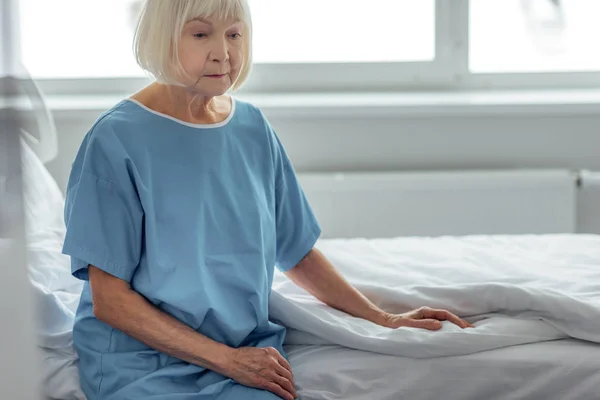 Lonely senior woman sitting on bed in hospital ward — Stock Photo