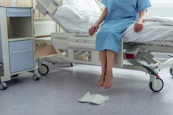 Частичный взгляд пожилой женщины, сидящей на кровати в палате больницы — стоковое фото