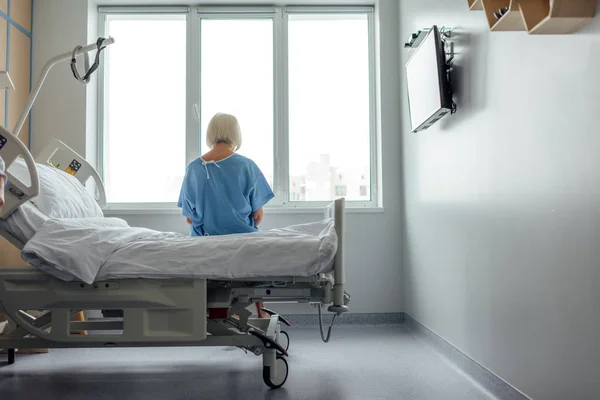 Back view of lonely senior woman sitting on bed in hospital ward with copy space — Stock Photo