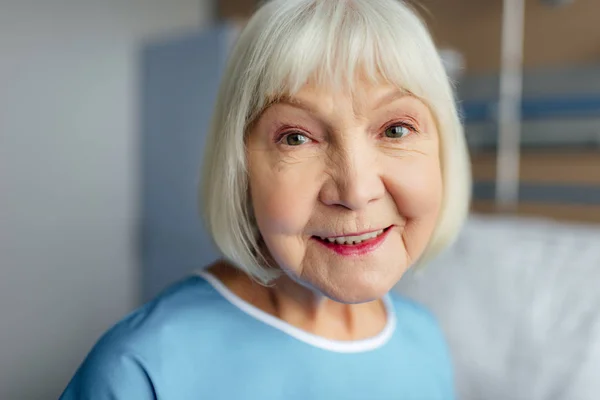 Retrato de mulher idosa feliz com cabelos grisalhos olhando para a câmera no hospital — Fotografia de Stock