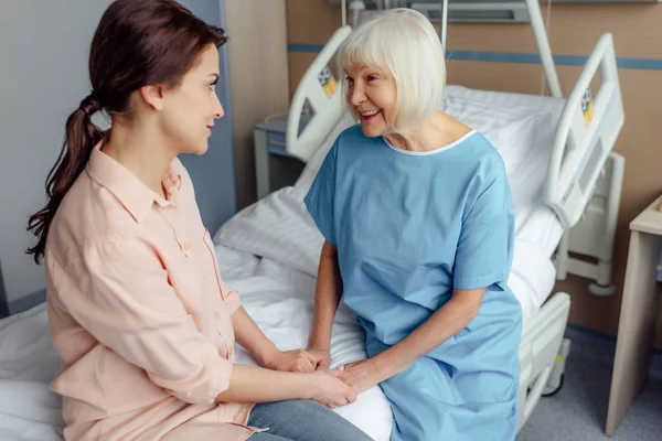 Senior woman and daughter sitting on bed and holding hands in hospital — Stock Photo