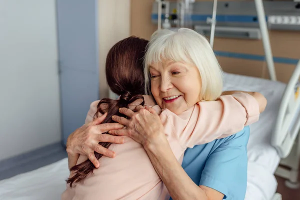 Heureux senior femme et fille assis sur le lit et câlins à l'hôpital — Photo de stock