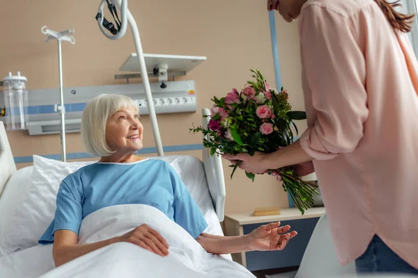 Дочь, дарящая цветы счастливой пожилой женщине в больнице — стоковое фото