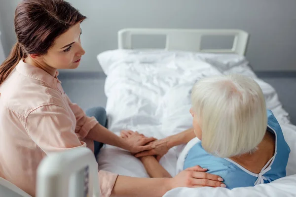 Селективное внимание пожилой женщины и расстроенной дочери, держащейся за руки в больнице — стоковое фото
