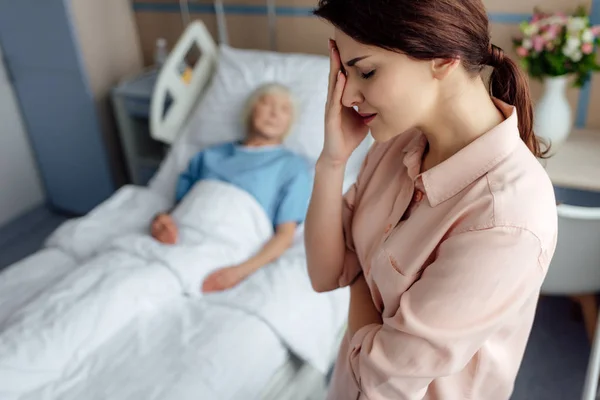 Foco seletivo da filha preocupada com a mãe doente na cama em segundo plano no hospital — Fotografia de Stock