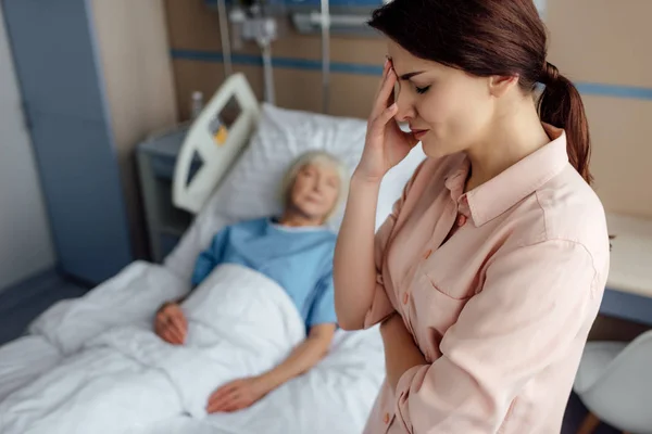 Selektiver Fokus der aufgebrachten Tochter mit kranker Mutter im Bett auf Hintergrund im Krankenhaus — Stockfoto
